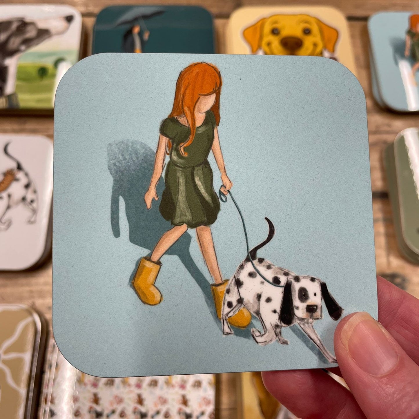 Coaster with illustration of a woman walking a Dalmatian dog, held over other coasters.