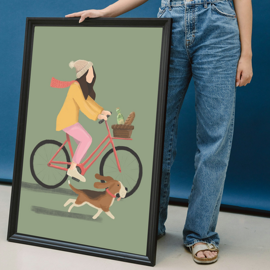 Person holding a framed illustration of a woman riding a bike with a dog on a green background