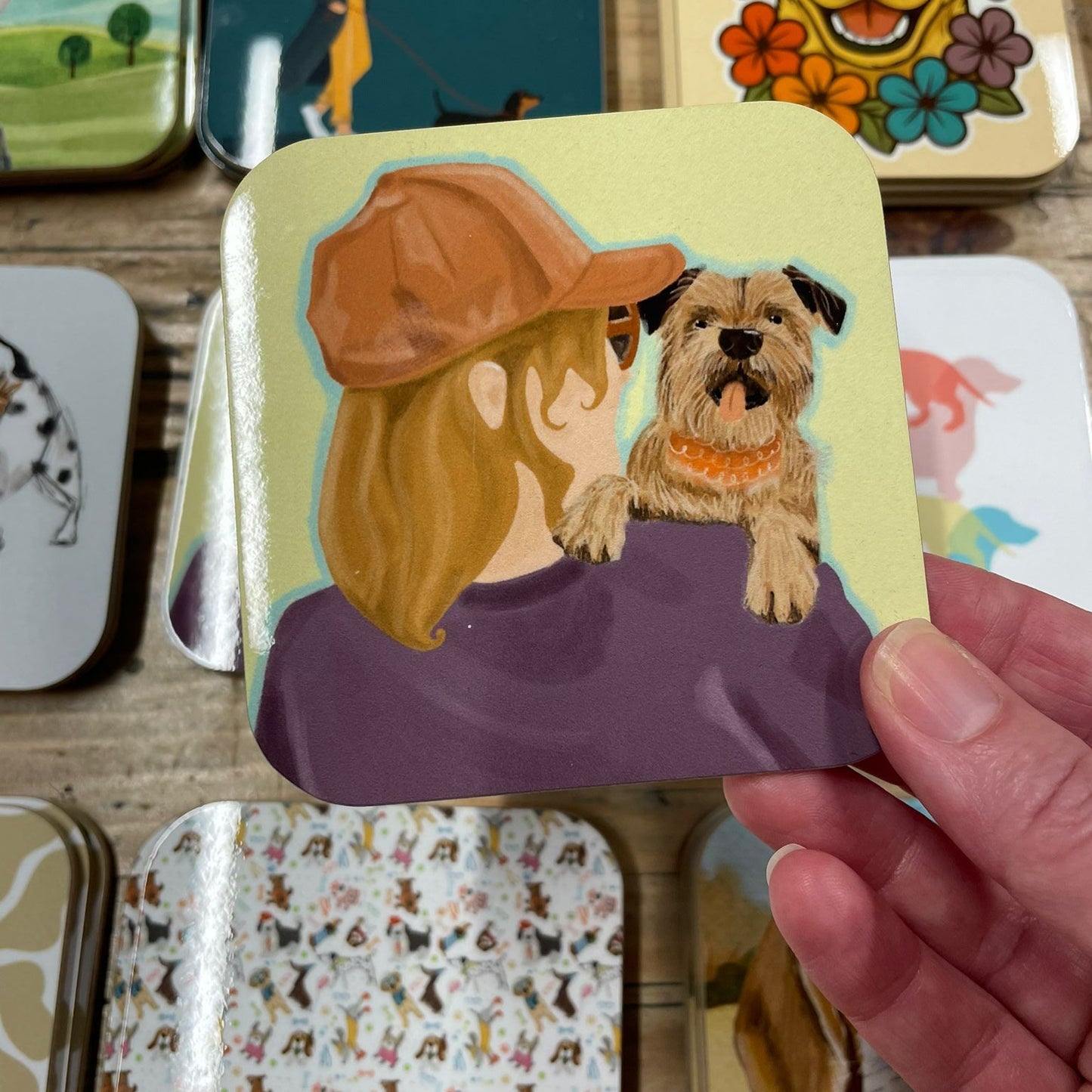 Hand holding a card with an illustration of a person and a dog, surrounded by other similar cards on a wooden surface.