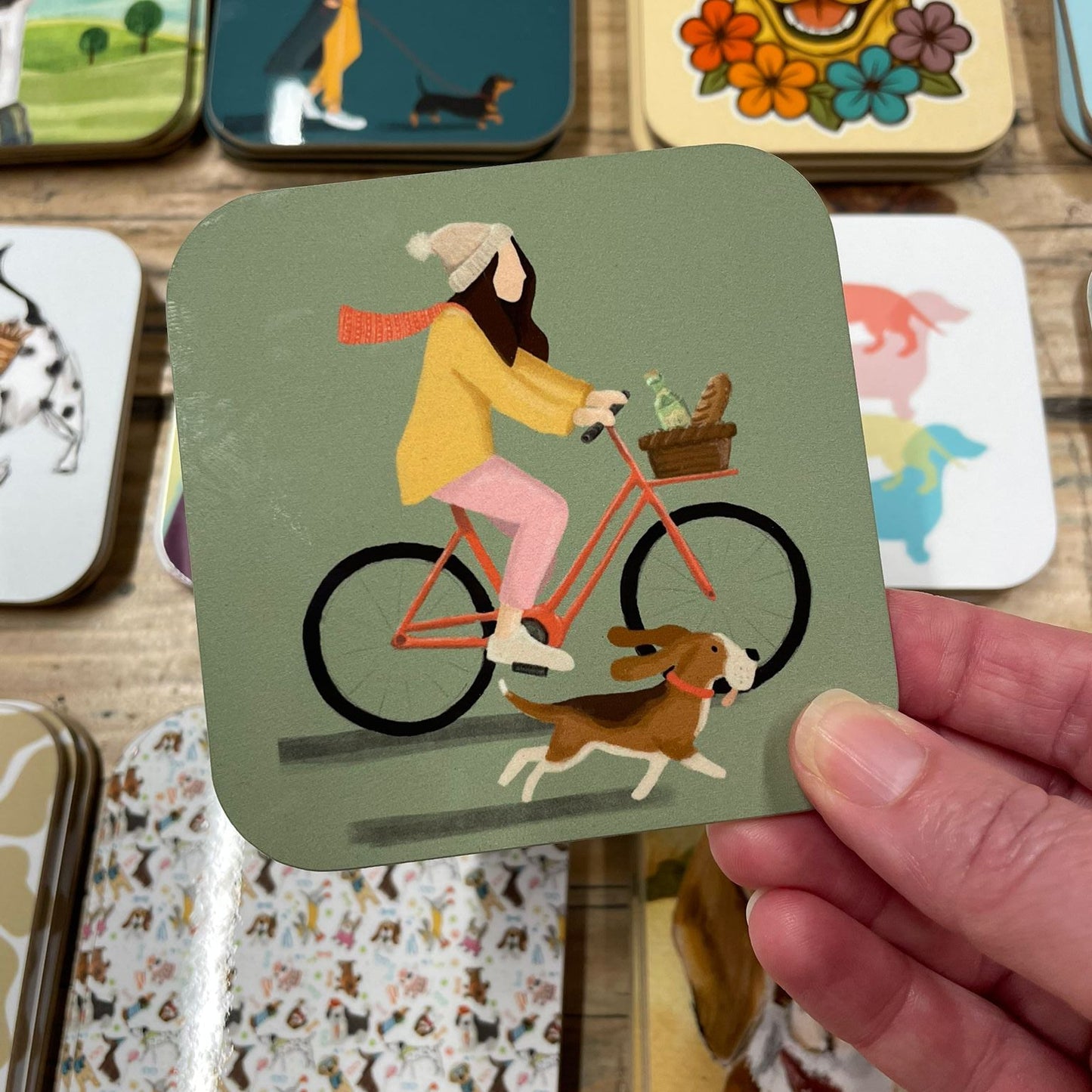 Card with a design of a person riding a bike with a dog on a wooden surface with other cards featuring animal illustrations.