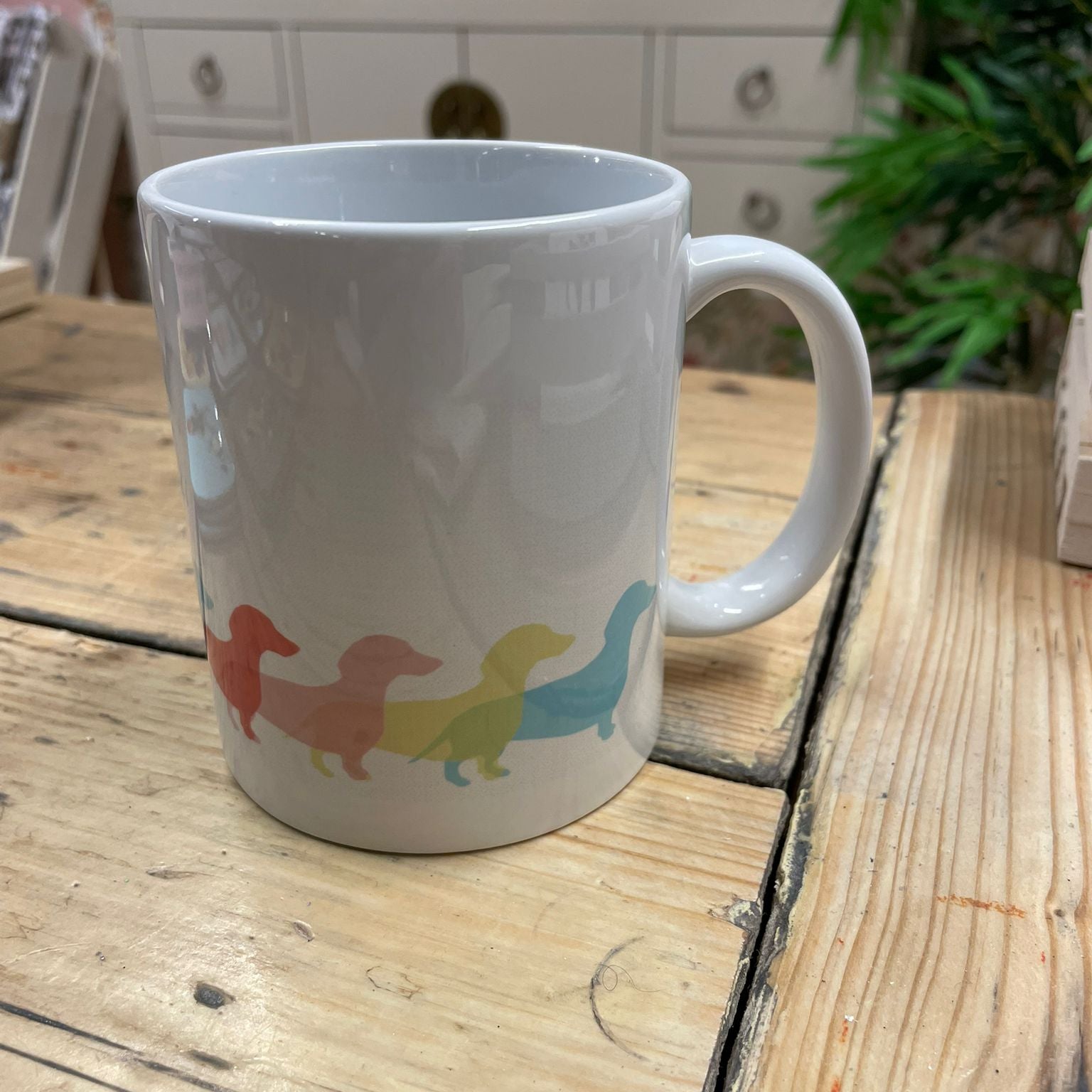 White mug with colorful dachshund design on a wooden surface