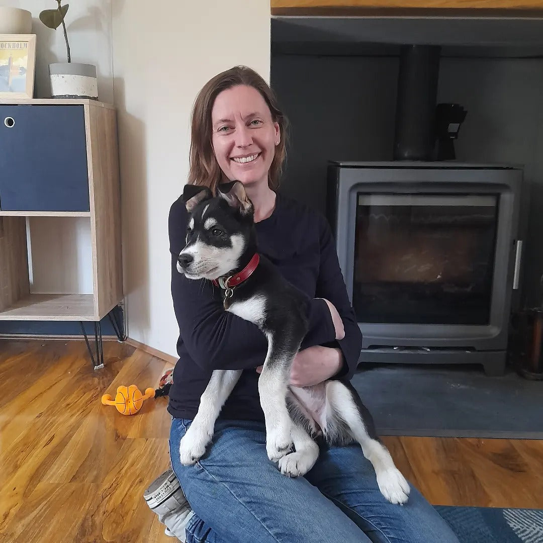Woman holding a small black and white dog in a living room with a fireplace.
